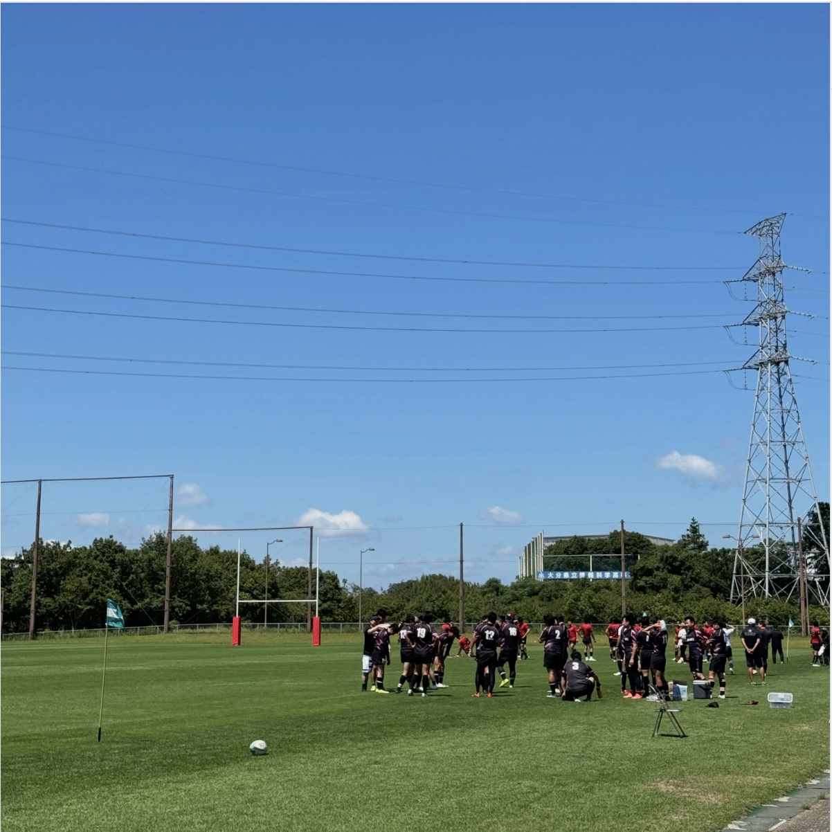 AGRIFALLS R.F.C. — 青空のもと、鉄塔を背景にラグビー場で夏季大会に向けて練習中のチーム
