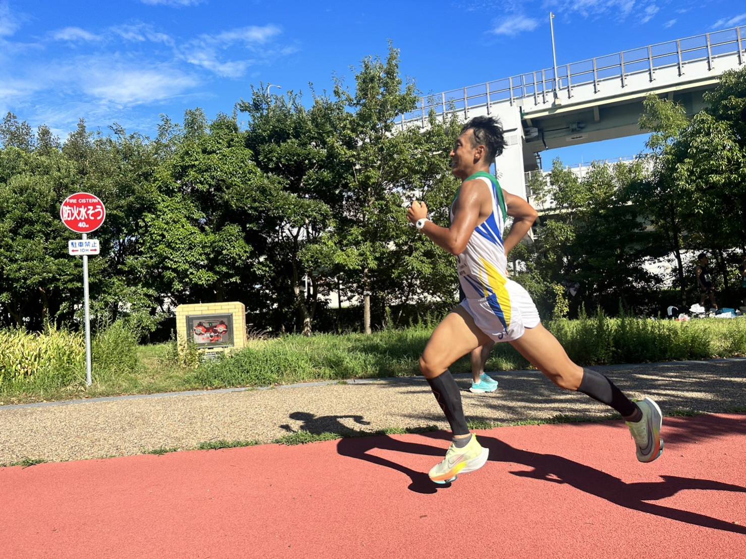 KOBE AC のシャツで走者が公園のランニングコースを疾走する。
