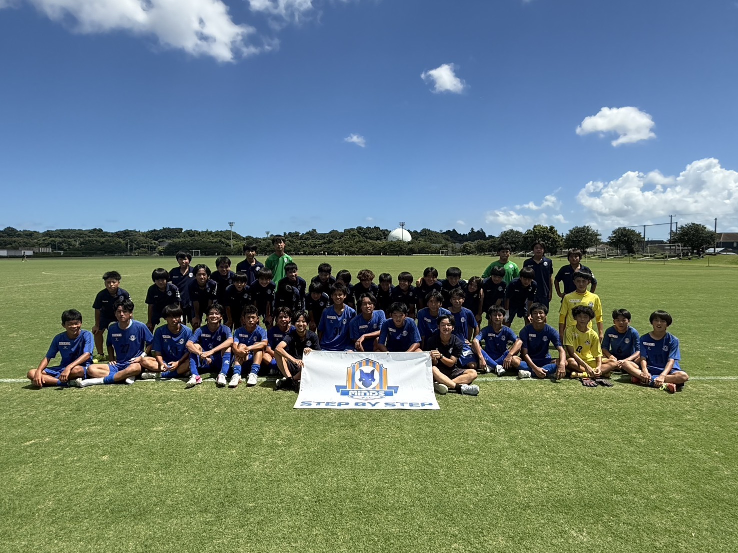 MINDS CHIBA FC の全体集合写真。中央に『STEP BY STEP』と刻まれたチームバナー。