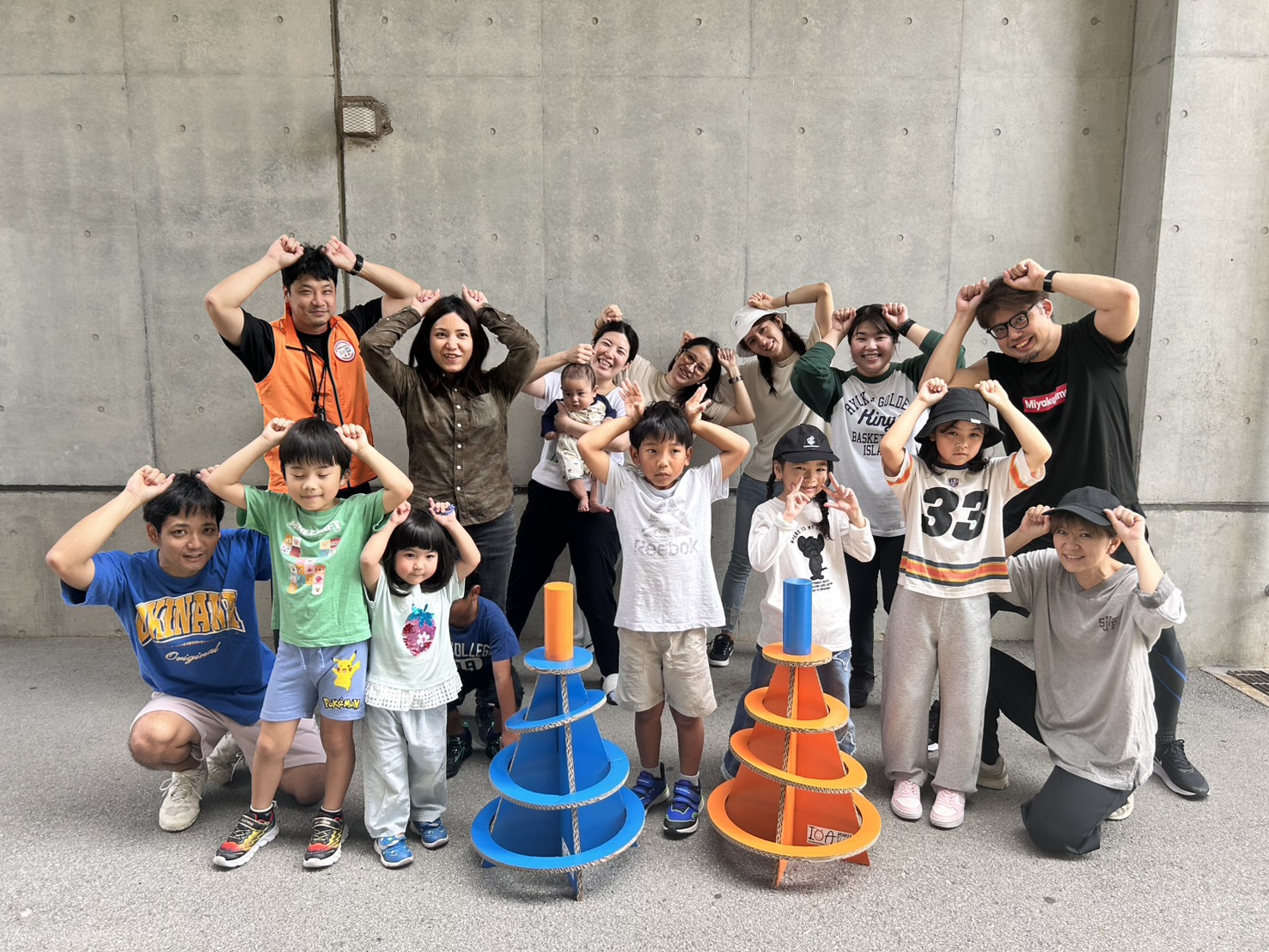 沖縄市スポーツ鬼ごっこ愛好会 — コンクリート壁の前で子どもも大人も鬼のポーズで並ぶ集合写真