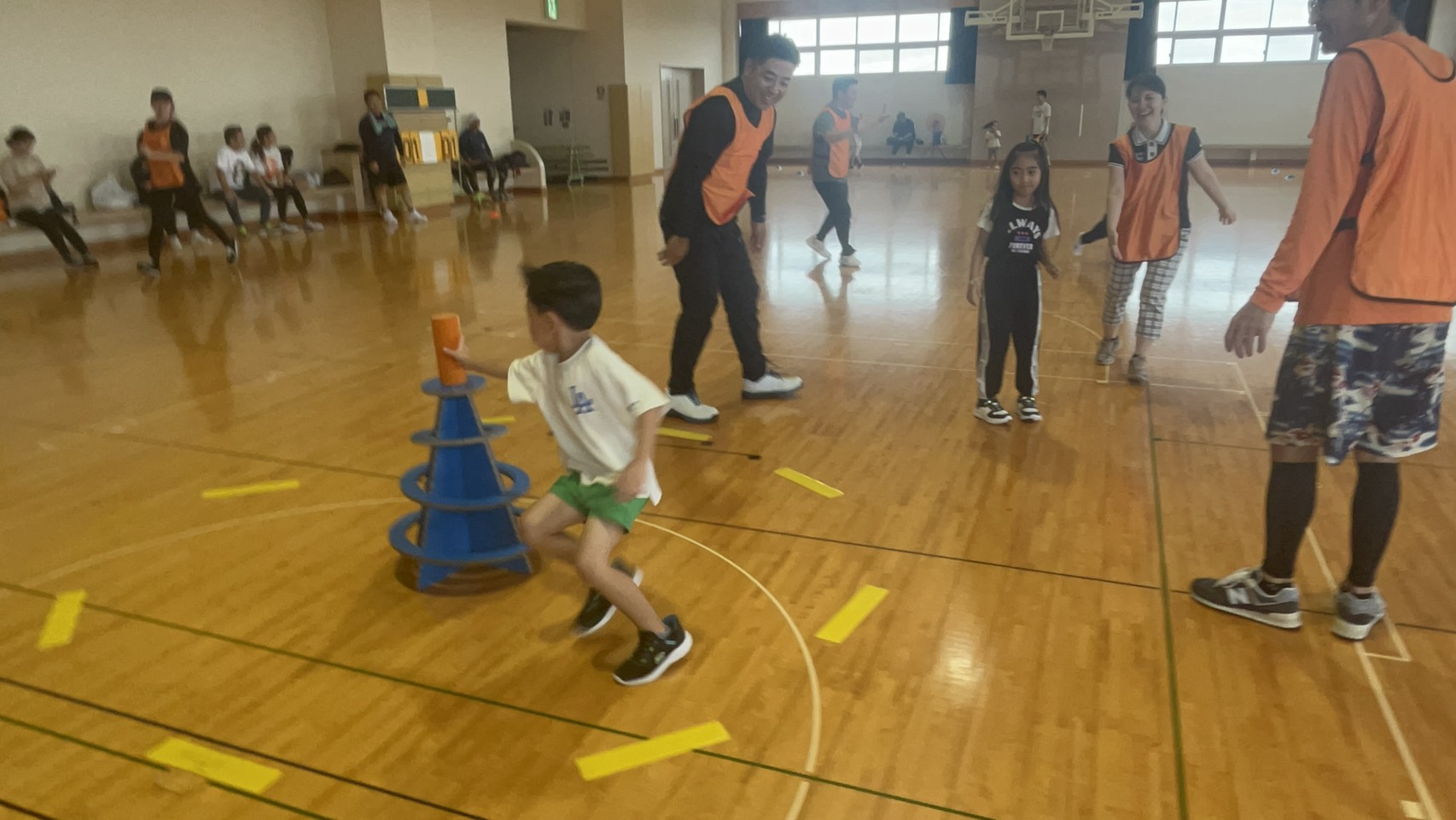 スポーツ鬼ごっこ — 体育館でオレンジのコーンを掴んで走り抜ける子ども