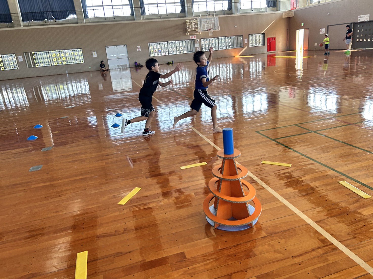 スポーツ鬼ごっこ — 体育館で2人の子どもが並走しながらSpooniゴールを目指す