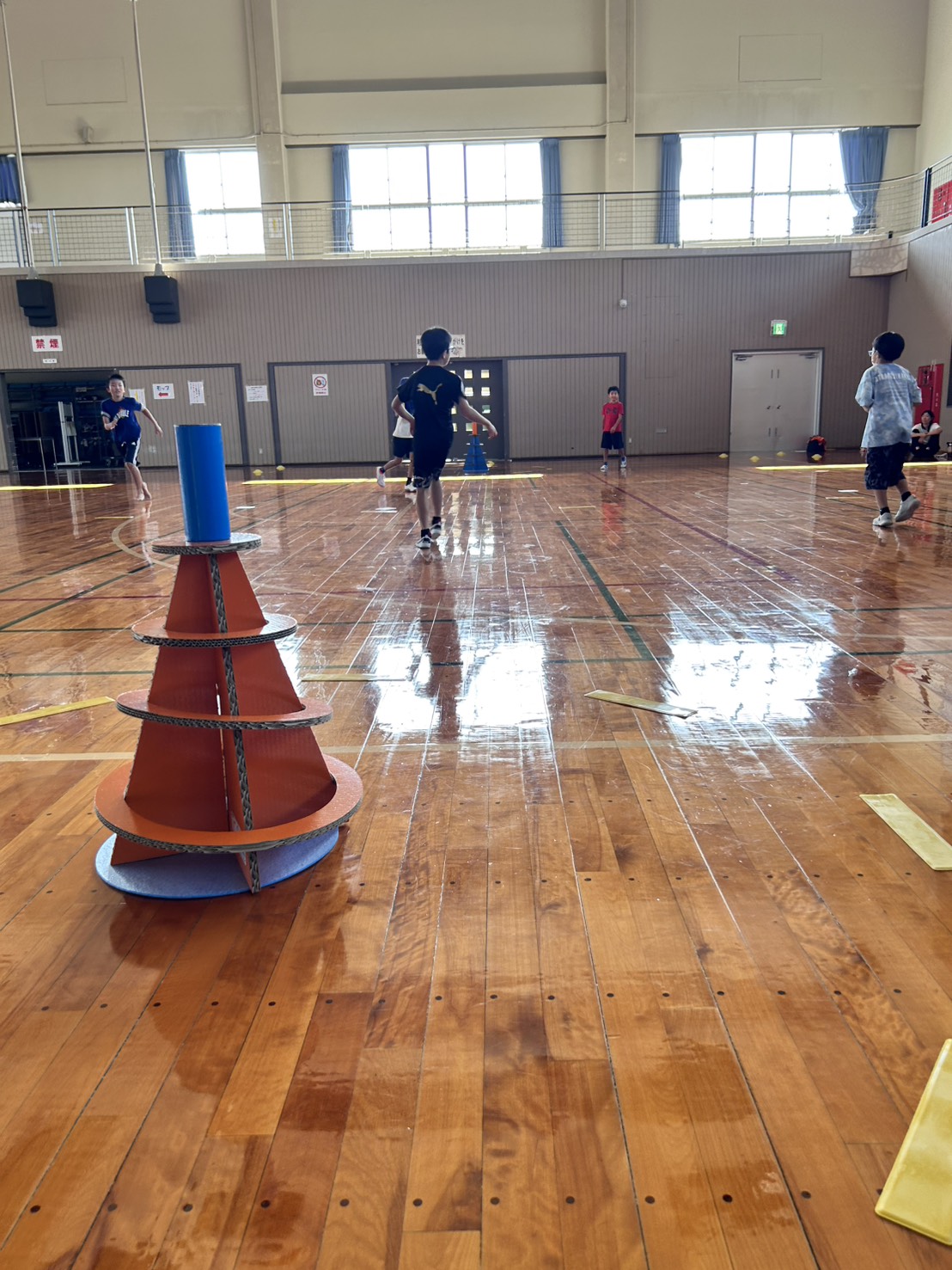 スポーツ鬼ごっこ — 体育館の床にそびえる青×オレンジのSpooniゴール、奥では選手たちが走っている